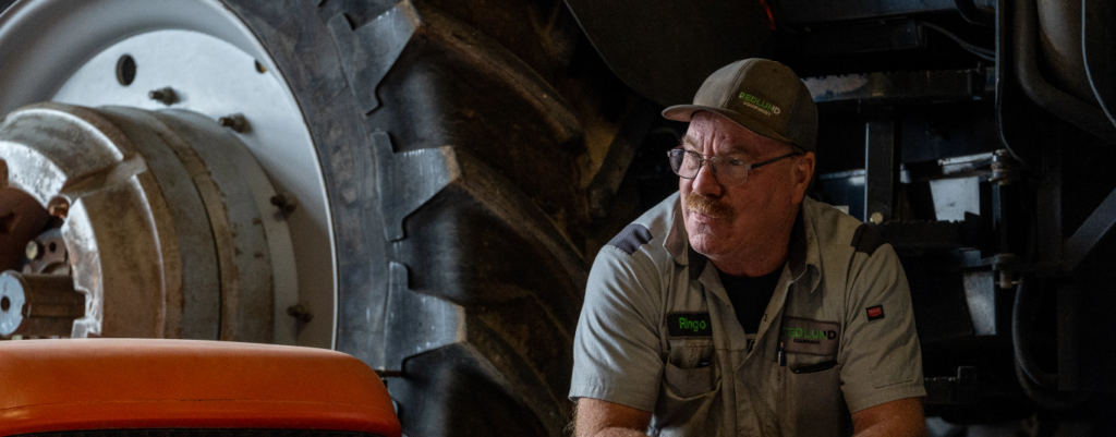 Service mechanic sitting in front of tractor tire 
